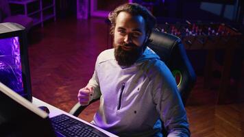 Professional gamer arriving in studio, greeting fans during livestream, talking about gaming systems. Man broadcasting from lit living room, engaging with viewers, discussing videogames topics photo