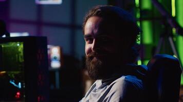 Man in dark living room playing games on gaming PC at computer desk during leisure time. Gamer battling enemies in online multiplayer shooter from neon lights ornate home photo