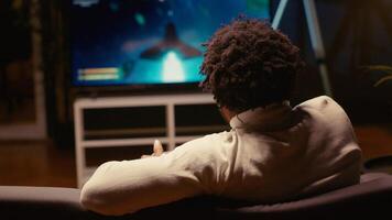 Man using cloud gaming service to play demanding science fiction videogame on large TV display. Gamer enjoying high quality graphics, streaming game online, handheld camera shot photo