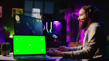 Chroma key laptop next to man playing high FPS singleplayer videogame with spaceship shooting lasers. Isolated screen notebook near gamer using crosshair to hit targets in SF game, zoom out photo