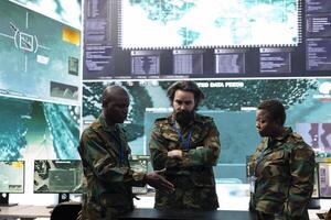 Diverse crew of soldiers gathering to discuss operations plan in control center, operating with a hologram to examine mission details. Troopers using 3d holographic projection for a briefing session. photo