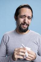 Male model dealing with a heartbreak and crying in studio, wiping his tears with a handkerchief and whining. Young sad man feeling unhappy and distraught, desolation and low self esteem. photo