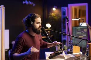 Young songwriter producer singing verses on microphone and adjusting volume levels on the melody, composing a new song with mixing console and daw software interface. Professional composer artist. photo