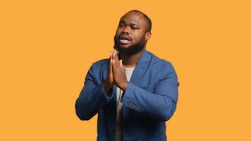 Friendly african american man puts hands together in apology gesture, asking for forgiveness. Apologetic BIPOC man doing sorry gesturing, asking for pardon, isolated over studio background, camera A photo