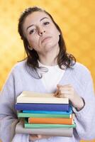 Portrait of woman carrying stack of books, gathering information for school exam, isolated over studio background. Student holding pile of books, preparing for university assessment photo