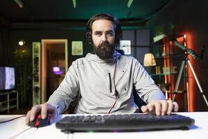 Pro player compets in intense online multiplayer videogame with his friends, shooting enemies from living room with rgb lights. POV of man using gaming computer and headphones for immersive experience photo