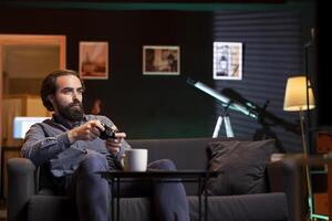Gamer playing videogames on console late at night in neon illuminated room, drinking coffee to stay awake. Man with caffeinated beverage in front using controller to finish game before going to sleep photo