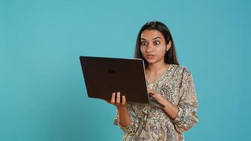 Woman composing email, carefully typing on laptop keyboard, struggling to think of what to write. Indian person sending mail online, brainstorming message idea, studio background, camera A photo