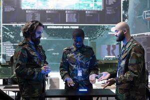 Team of diverse troopers collecting intelligence in a power base, studying CCTV footage on a hologram projection to aid infantry units in the field. Trained soldiers study real time data. photo