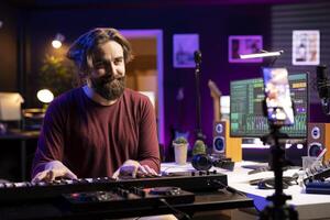 Singer hosting internet master class to teach piano lessons on social media, explaining electronic keyboard notes in home studio. Skilled artist playing on midi controller for online vlog. photo