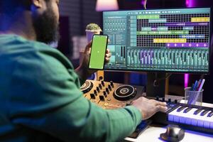Producer using stereo console to apply mixing and mastering techniques, having a copyspace display on his phone. Artist songwriter producing new soundtracks in home studio. photo