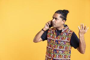 Disappointed indian man admonishing friend over debacle on call, negatively surprised by him, studio background. Upset person in disagreement with mate, rejecting arguments from his opponent photo