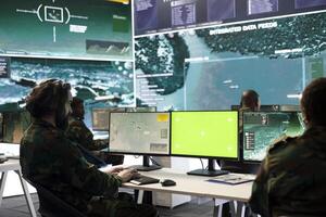 Army specialist operates on satellite radar surveillance and copy space screen, using real time information to aid troops in monitoring room. Young soldier follows GPS location on world map. photo