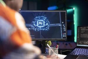 Professional male developer manages neural network at desk, working with AI code on laptop. African american IT expert freelancer developing cyber security, creating secure database. photo