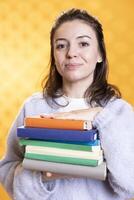 Portrait of smiling woman with stack of books in hands showing appreciation for literature, isolated over studio background. Happy bookworm holding pile of novels, enjoying reading photo