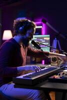 Audio engineer playing piano electronic keyboard to compose a new song, singing on microphone and adjusting volume levels. Producer recording music, plays on midi controller gear. photo
