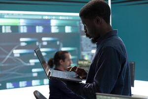 Governmental hackers breaching network security with advanced techniques, cyber defense in action. Team of IT experts working on gaining access to collect information, big screen. photo