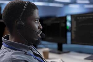 IT support worker in data center talking in headphones mic, doing yearly checkup to avoid equipment downtime. Employee chatting with on field engineer in server hub, monitoring servers infrastructure photo