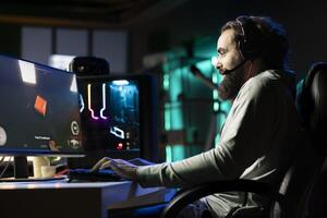 Popular streamer in neon illuminated studio chatting with audience, urging them to pick game for him to play. Pro gamer interacting with viewers watching his livestream, talking about videogames photo