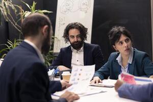 Project manager and his team gathering in a boardroom meeting, discussing all important statistics, giving insight and details to staff members before working on development planning. photo