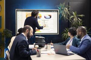 Marketing manager evaluating sales and profit within infographics data, coworkers sharing insight in a briefing conference. Team members planning promotional activities for a better public image. photo