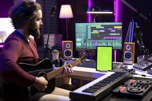 Composer playing acoustic guitar after following online tutorial, learning new strings accords in his home studio. Music producer learning to p lay a new melody on instrument, greenscreen layout. photo