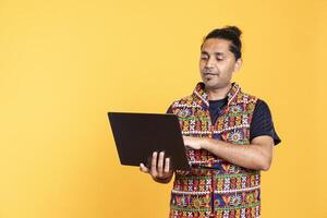 Indian man typing on laptop keyboard, doing job tasks for company, isolated over studio background. Worker inputting data on notebook device, working as office clerk, studio backdrop photo