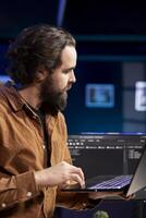 Computer engineer crosschecking between laptop and monitor, implementing security measures to protect company systems. IT worker comparing software code between notebook and PC photo
