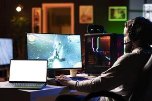 Isolated screen laptop next to man having fun by using gaming keyboard to fly spaceship in SF videogame. Mockup notebook device next to gamer using powerful PC and computer peripherals to play game photo