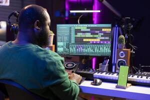 Songwriter working on making new music with a greenscreen on phone, operating on mixing console and professional software. Skilled artist producing and editing soundtracks in home studio. photo