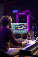 Audio engineer operates mixing equipment and oversees recordings performances to ensure the perfect tunes. Artist producer composing sounds with MIDI controller piano and electronic console. photo