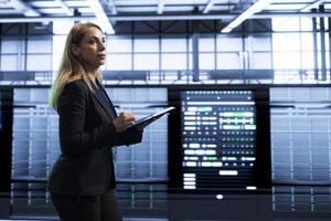 Manager in server room using tablet to implement and maintain security measures, protecting systems from unauthorized access. Woman in data center doing hardware maintenance with device photo