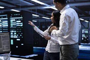 Engineering colleagues in data center looking for firewall misconfigurations affecting servers, doing brainstorming. System administrators in server room checking systems bottlenecks photo