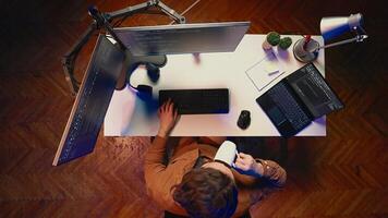 Top down view of self employed man doing IT support job from apartment personal office, coding on PC, drinking coffee. Software developer writing lines of code on computer at home, aerial shot photo