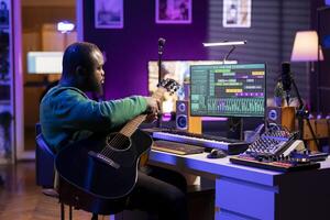 Creative songwriter singing a melody and playing guitar, signal processing technology with digital audio software. Artist producer creating music with acoustic instrument and console. photo
