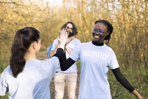 Satisfied diverse women sharing a high five feeling proud of their hard work to clean the natural habitat. Congratulating each other for showing perseverance and devotion. photo