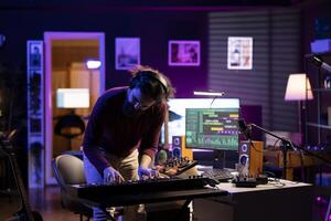 Cheerful artist playing music on electronic keyboard in home studio, recording new songs and having fun with audio session. Confident musician plays tunes on piano midi controller. photo