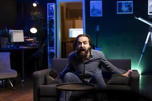 Ecstatic sports fan watching live match broadcast in apartment, shouting to celebrate favorite team scoring. Euphoric man yelling, delighted about goal, happy with own country triumph in tournament photo