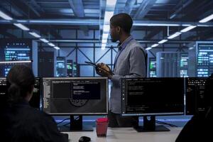 Admin in data center using tablet to check for server performance issues arising due to high CPU usage. Server room employee fixing insufficient memory errors slowing down hardware photo