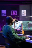 Sound producer working with console and electronic keyboard to create the perfect tracks for his songs, recording and editing audio. Music composer adjusts volume levels on pre amp knobs. photo