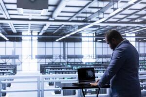 System administrator programming in AI data center housing advanced equipment used for machine learning training. Server hub employee runs code on notebook to upgrade artificial intelligence systems photo