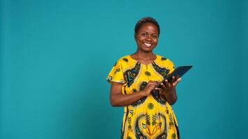 Natural cute girl browsing internet on a tablet against blue background, navigating on online web pages by using a portable device. Woman posing with a gadget and traditional outfit. Camera B. photo