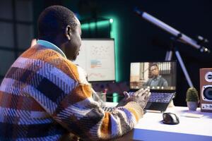 Black man waving on call and discussing about business infographics, reviewing monthly budget balance and working remotely. Staff focused on conversation during online meeting on pc. photo