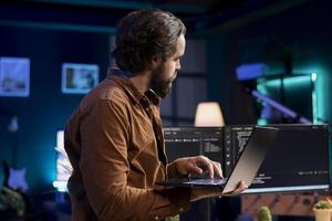 Man doing software quality assurance, reading source code on laptop, crosschecking with computer monitors. IT admin inspecting coding on notebook device, using PC screens at reference point photo