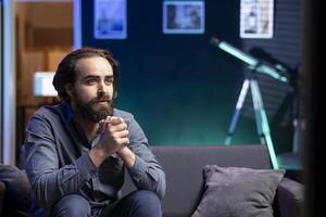 Homeowner at home using TV to watch romantic movie on subscription based streaming services. Man sitting on couch showing endearment emotions, enjoying VOD shows on television display photo