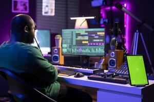 Producer editing his audio files and recordings on digital pc interface, sitting next to an isolated mockup screen. Talented sound engineer mixing and mastering songs with console in home studio. photo