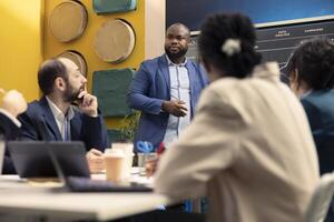 General manager sharing insight about a new marketing strategy with his staff members, presenting infographics and sales data reports on interactive board. Coworkers in a conference room. photo