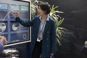 Woman consultant examining monthly sales infographics on interactive board, reviewing feedback on previous initiatives for future improvements. Management team in a conference. photo