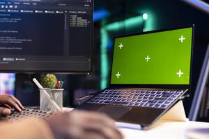 African american programmer working on cloud computing next to green screen, writing code for optimization on terminal window. IT engineer works to insert html code, server security. photo