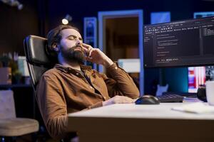 Programmer suffering from headache while filtering malicious traffic from cybercriminals attempting to steal company data. Stressed man hurting from pain and overworking, preventing malware photo